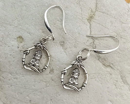 A pair of silver-toned dangle earrings with small hanging charms, displayed on a light gray stone surface against a white background.